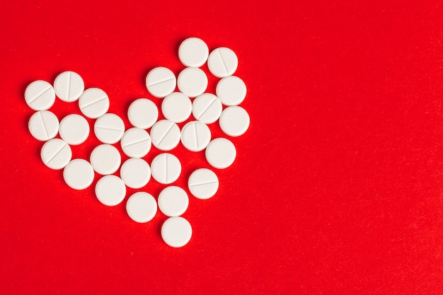 Pills heart out of pill bottle on red, top view 