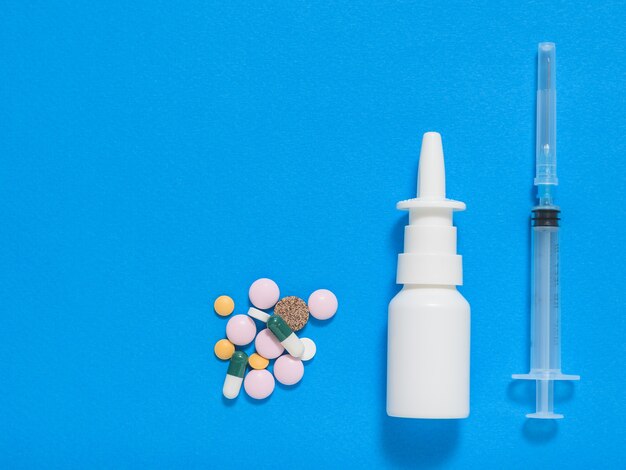 Pills, nose spray and syringe on blue background. A set of medicines for the treatment of diseases.