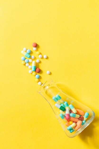 Таблетки и флаконы с таблетками на желтом фоне, разноцветные таблетки и капсулы с таблетками из стеклянной бутылки