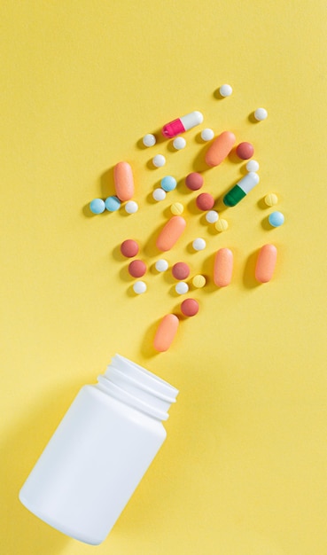 Pillole e flaconi di pillole su sfondo giallopillole mediche sparse da un tubo bianco su un giallo