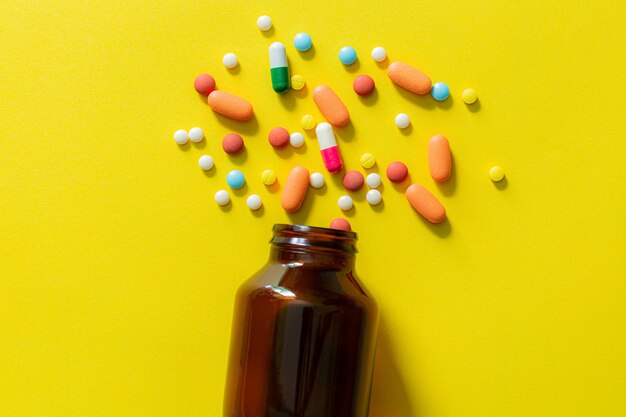 노란색 배경에 있는 알약과 알약 병 유리병에서 여러 가지 빛깔의 정제와 알약 캡슐