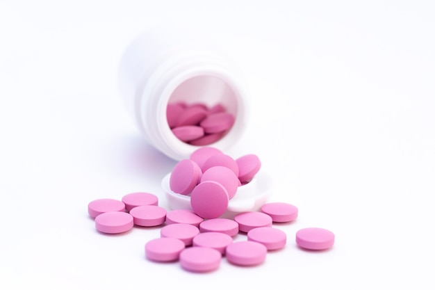 Pills of pink color from a white jar on a white surface. The concept of health care, treatment, illness.