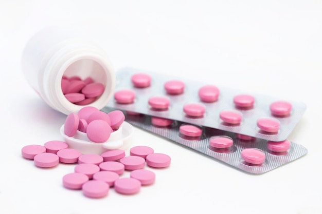 Pills of pink color from a white jar on a white surface. The concept of health care, treatment, illness.