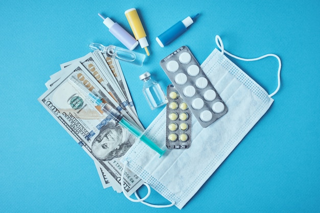 Pills, protective mask, medical items and dollar bills on blue