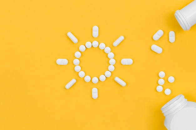 Pills in the shape of the sun on a yellow background flat lay