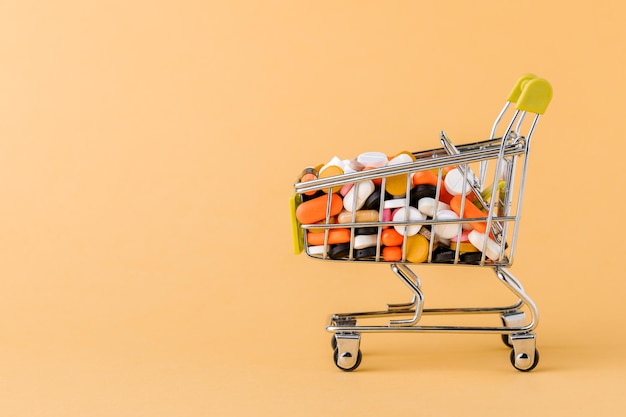 Photo pills and shopping cart on a yellow background concept of buying drugs, prices for treatment. sale in the pharmacy.