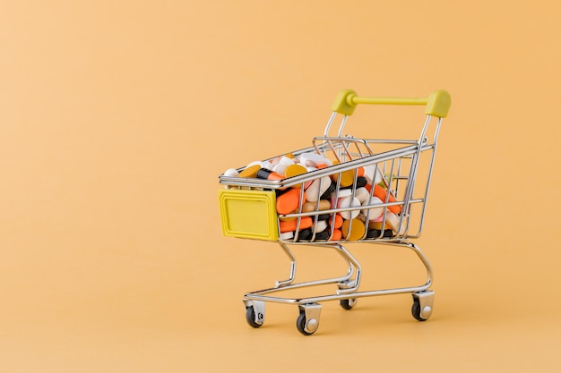 Photo pills and shopping cart on a yellow background concept of buying drugs prices for treatment sale in the pharmacy