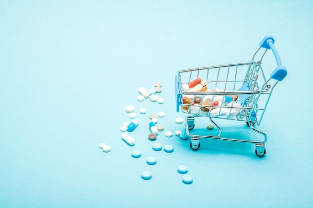 Pills and Shopping trolley on blue background. Creative idea for health care cost, drugstore, health insurance and pharmaceutical company business concept. Copy space.