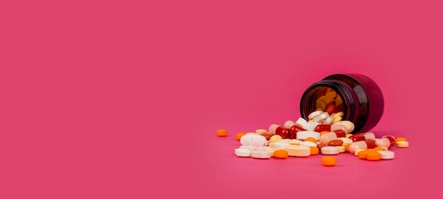 Pills spilling out of orange glass bottle isolated on pink background with copy space