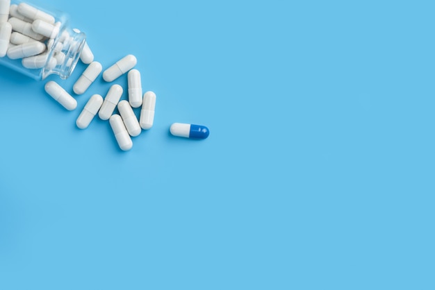 Pills spilling out of pill bottle of a glass bottle. pharmaceutical medicine tablets on the blue background