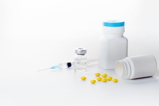 Pills spilling out of pill bottle syringe thermometer and stethoscope on white background