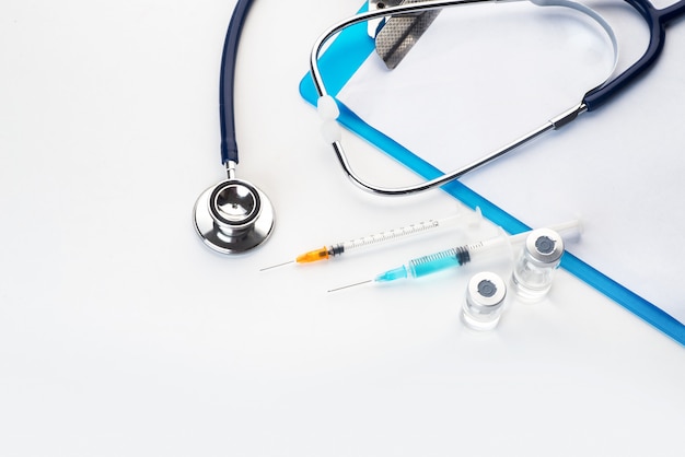 Pills spilling out of pill bottle syringe thermometer and stethoscope on white background