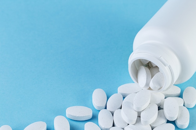 Pills spilling out of white bottle on blue background