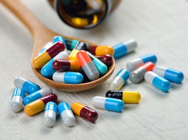 Pills in the spoon on white wooden surface