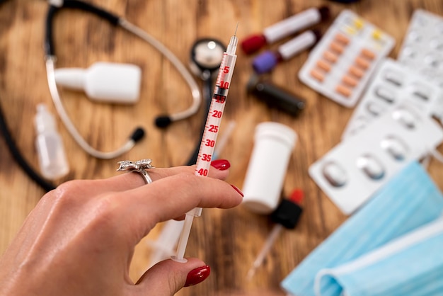 Pills stethoscope blood flasks masks on the side of a woman's hand holding a syringe