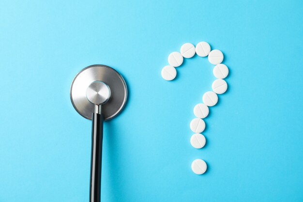 Pills and stethoscope on blue background, close up