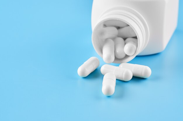 Pills tablets capsules closeup. On a blue background, a jar of medicine.