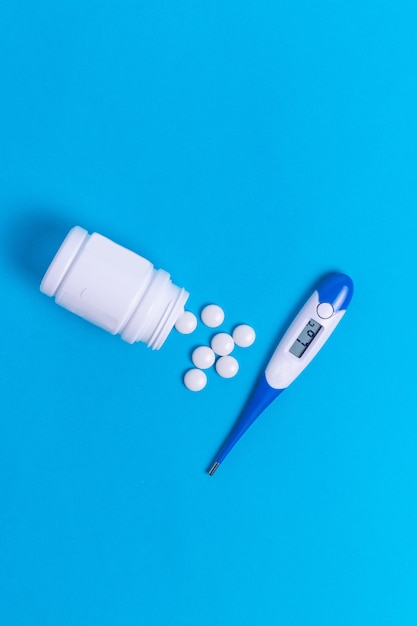 Pills and thermometer disease virus treatment on blue background