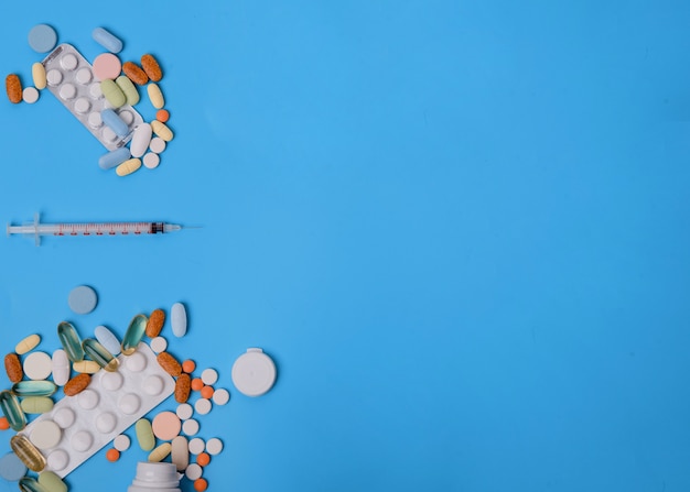 Pills, vitamins and disposable syringe on blue background Space for text