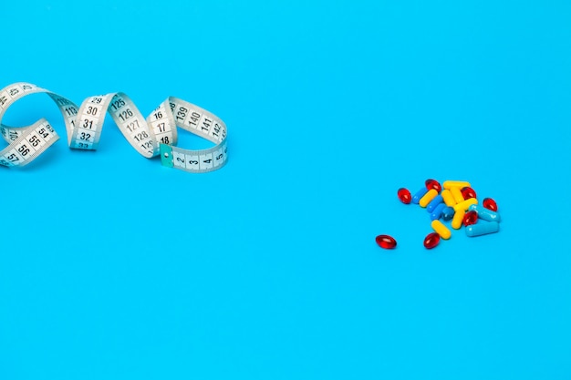 Pills for weight loss and tape measure on blue.