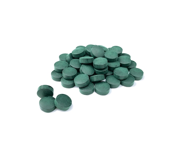 Таблетки на белом фоне из сине-зеленых водорослей спирулины с легкой тенью.