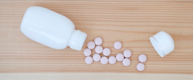 Pills in a white jar were scattered on the wooden background of the table. Concept of treatment of diseases. Destruction of the body, harm from pills.