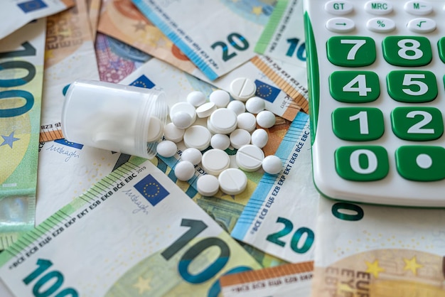 Pillole con calcolatrice sul mucchio di soldi in euro come concetto di sfondo di alto costo della farmacia