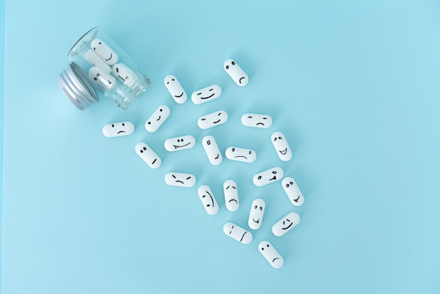 Pills with funny faces and a glass bottle on a blue background