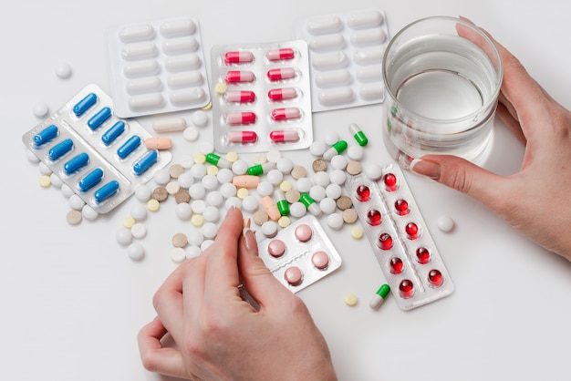 Pills with glass of water and hand holding pill.