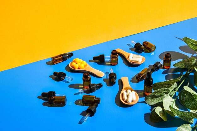 Таблетки на деревянной пипетке ложки и капельницы на синем и желтом фоне. Жесткий свет и тени. Современная изометрическая концепция творческого минимализма. Витамины и пребиотики, пробиотики. Осенняя доза витаминов.