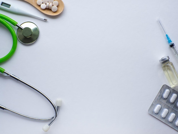 pills in wooden spoon thermometer stethoscope and syringe on white background