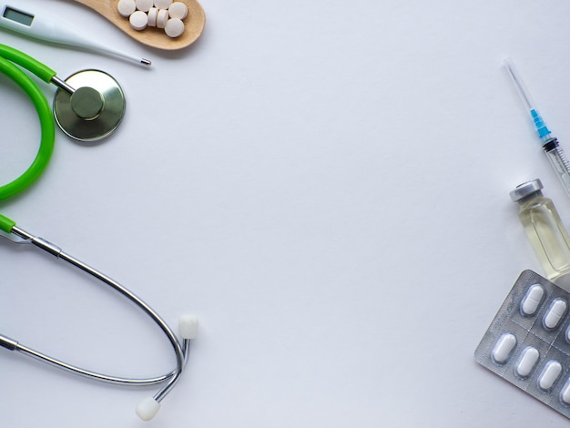 Pills in wooden spoon thermometer stethoscope and syringe on white background