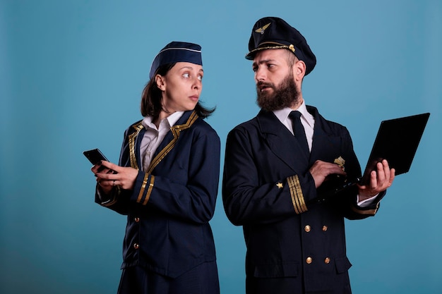 Pilot using laptop, flight attendant messaging on smartphone.\
airlane captain in professional uniform holding portable computer\
in airport, air hostess browsing internet on mobile phone