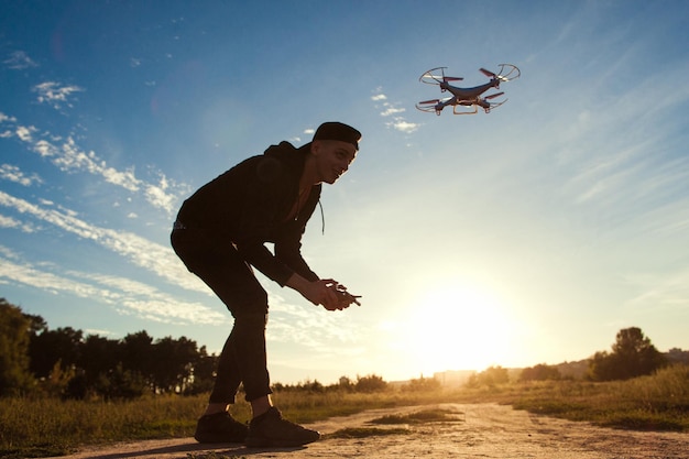 Piloting drone in field sunset flare free space Young man running quadrocopter outdoor on blue sky background Leisure entertainment modern technologies concept