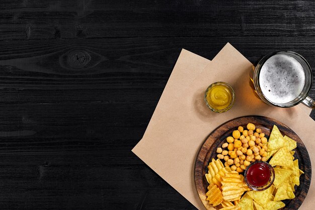 Pils bier en snacks op zwarte houten tafel noten chips bovenaanzicht met copyspace