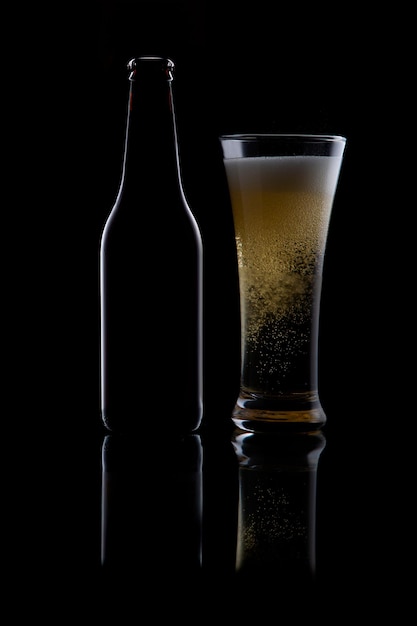 Pilsner glass and bottle in black background on reflective base