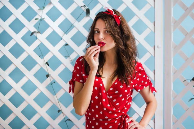 Pin-up girl in a red dress eats juicy strawberries