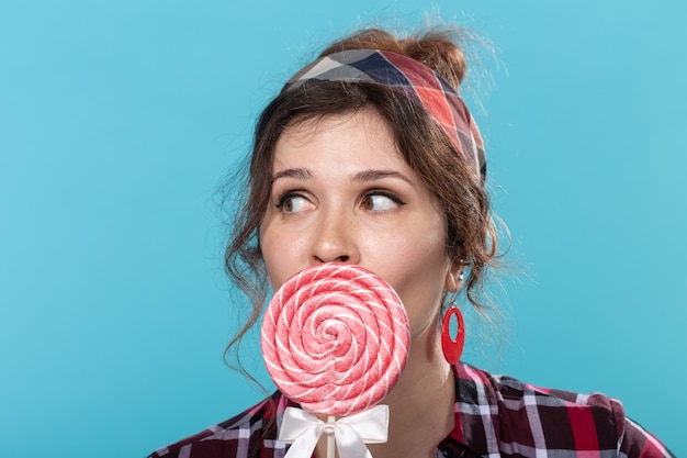 Photo pin-up woman, fashion and people concept - portrait of pin-up woman with lollipop over the blue background.