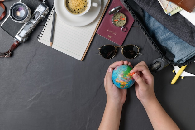 세계 지도에 핀을 고정하고 검은색 배경에 가방, 빈티지 카메라, 노트북, 여권, 지도, 뜨거운 커피를 준비하세요. 여행 컨셉