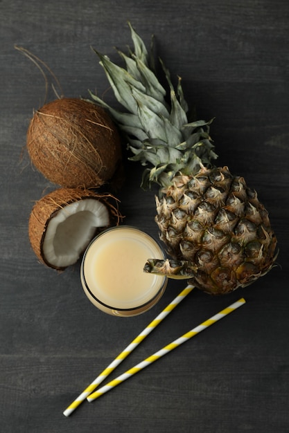 Pina colada cocktail and ingredients on dark wooden table.