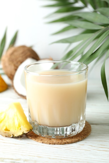 Pina colada cocktail and ingredients on white wooden table.