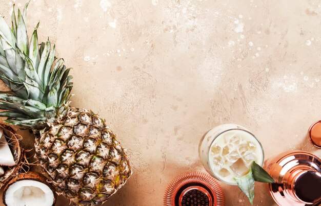 Pina colada cocktail on sand beige background with tropical fruits and bar tools summer relaxation concept Top view copy space