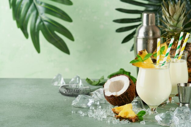 Pina Colada Traditional caribbean cocktail from rum pineapple juice and Coconut cream with tropical fruits and bar tools on fresh green background Summer tropical cocktail and relaxation concept