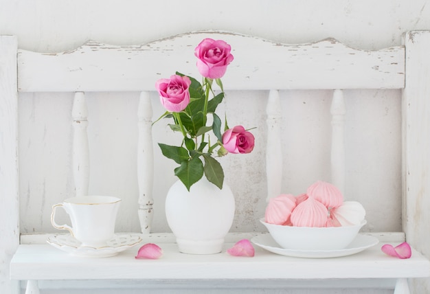 Pinc roses in vase and dinnerware on white wooden shelf