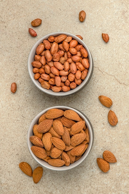 Pinda's en amandelen in kopjes op een marmeren tafelblad, bovenaanzicht. Superfoods en gezond eten concept.