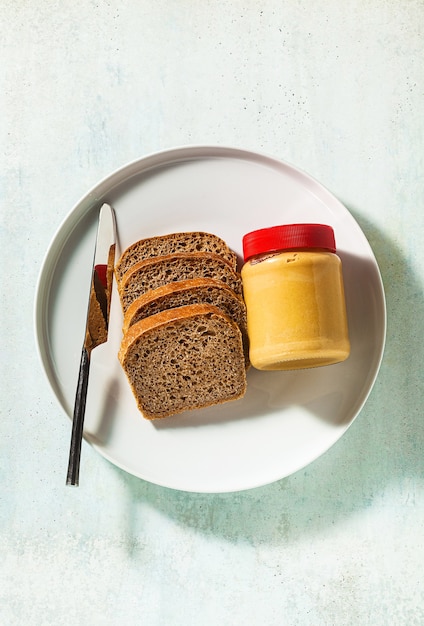 Pindakaas in een pot en volkorenbrood met een mes op tafel.