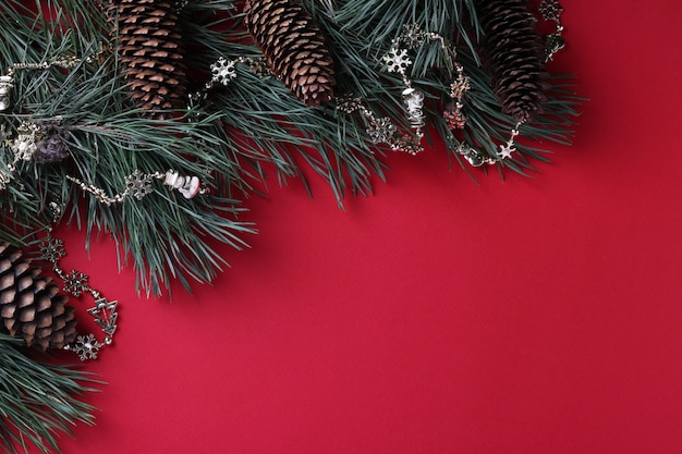 Pine branches with cones and garland on red surface. Space for wishes.  Top view. Space for wishes