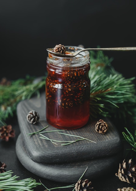 Pine cone jam in a glass jar against the background of pine branches and cones