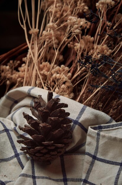 A pine cone sits in a basket with a plaid cloth.