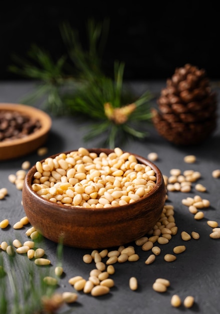 Pine nuts cedar in a bowl and a handful of unpeeled nuts on a gray background with a branch of pine needles Healthy diet snack